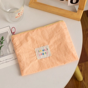 Macro shot of an orange-pink nylon cosmetic bag with a decorative lettered patch and zipper