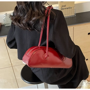 Detail of glossy burgundy underarm bag shown on model in a stylish cafe setting
