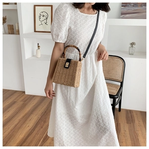 Detail of handmade straw handbag with bamboo handle and leather strap in a minimalist room