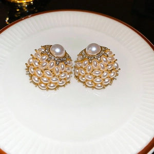 Macro shot of gold floral earrings with faux pearls and sparkling zircon on white ceramic