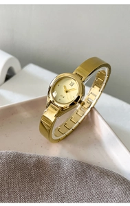 Detailed close-up of a gold bangle watch with metal chain strap on a pink ceramic dish
