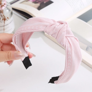 Vue détaillée du bandeau en tissu rose avec broderies de feuilles et nœud central