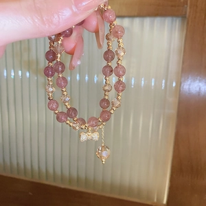 Detailed shot of double-layer pink beaded bracelet with a gold rhinestone bow pendant