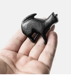 Close-up of black cast iron cat-shaped drawer handle held in hand showing texture