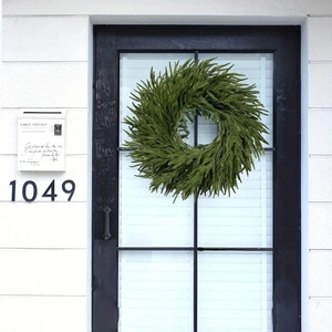 Close-up of artificial green fern wreath hanging on a white shutter door for home decor