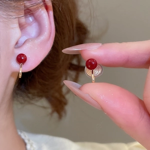 Detailed view of red round clip-on earrings with gold finish on earlobe and hand