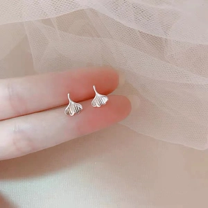 Macro detail of silver ginkgo leaf stud earrings held by fingers to show small size
