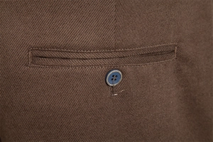 Close-up of a welt pocket and dark button on brown twill fabric for casual trousers