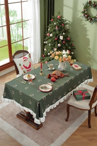 Detailed view of dark green Christmas tablecloth with white ruffled hem and holiday prints