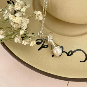 Macro shot of silver pearl necklace with a vintage bell-shaped pendant on a ceramic dish