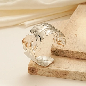Macro detail of leaf-shaped silver metal bangle resting on a textured stone surface