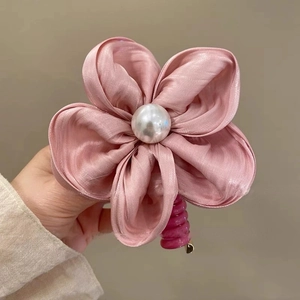 Gros plan détaillé d'un accessoire à cheveux fleur en satin rose avec perle centrale
