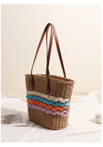 Detail of straw tote bag with rainbow woven stripes and brown leather handles on white cloth