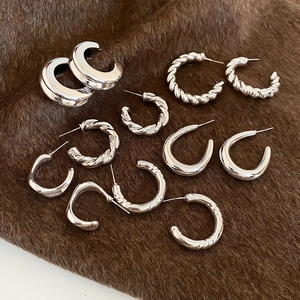 Macro detail of silver geometric C-hoop earrings featuring textured and polished finishes
