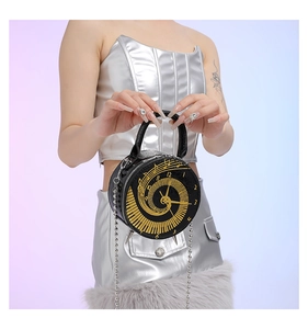 Detail of round black handbag featuring gold clock face dial and metal chain strap