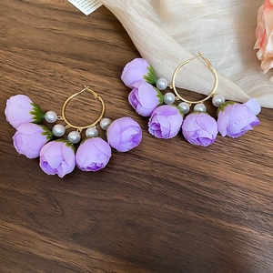 Detailed close-up of purple fabric rose hoop earrings with pearls on a dark wood background