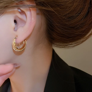 Macro shot of minimalist gold triple layered crossover hoop earrings on model ear