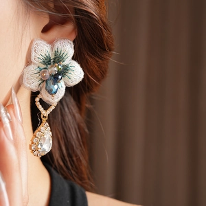 Gros plan sur la boucle d'oreille fleur en tissu blanc vintage avec pendentif en cristal