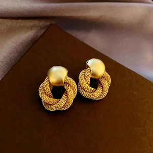Macro detail of gold-plated geometric earrings with matte finish and woven metal texture