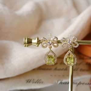 Detail of gold bow earrings with a pale green water-drop stone on a display stand