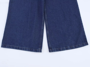 Gros plan d'un jean bleu foncé montrant les coutures de l'ourlet et la texture du tissu