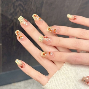 Detail van handgemaakte kunstnagels met gouden glitters en oranje bladvormige edelstenen