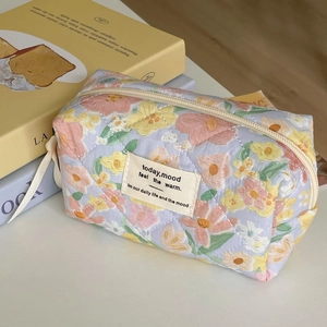 Detail showing the floral quilted makeup bag with soft pastel flowers and zipper closure