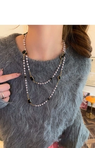 Double-layer long pearl necklace with black geometric pendants worn on a sweater