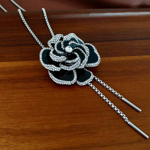 Macro view of black enamel camellia pendant with rhinestones and silver chain detail