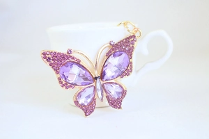 Detailed macro shot of purple crystal butterfly keychain with golden metal clasp and rhinestones