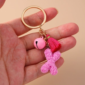 Pink floral letter X keychain with bell and tassel charm held on pink background