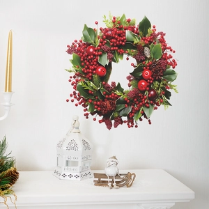 Couronne de Noël avec baies rouges, pommes de pin et feuilles sur un mur blanc déco