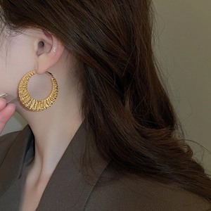 Detailed view of large gold twisted hoop earrings with textured finish on a model