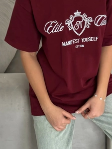 Détail de la broderie blanche et du graphique de bouclier sur un t-shirt en coton bordeaux
