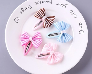 Detailed view of four colorful striped ribbon bow hair clips for girls on a white plate