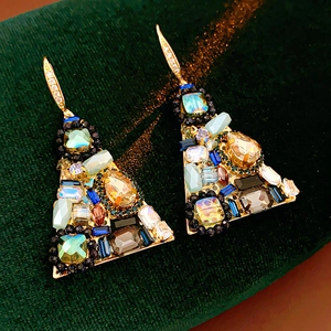 Close-up of golden triangle earrings with colorful zircon stones on green velvet