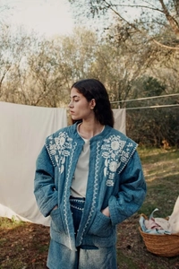 Detail of vintage blue denim jacket with intricate white floral embroidery and quilted texture