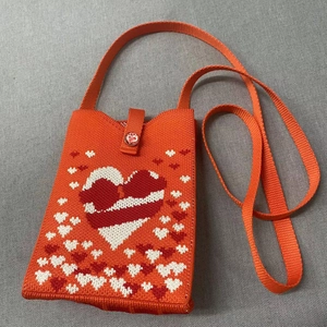Detail of orange knitted crossbody bag with pixelated heart patterns and button closure