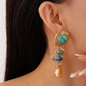 Gros plan de boucles d'oreilles vintage en résine avec pompons vert émeraude et dorés