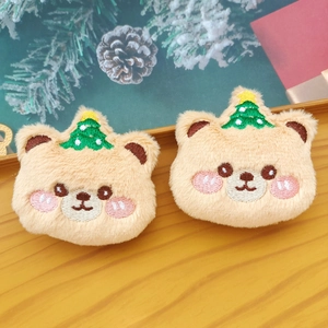 Detail of plush khaki bear accessories with embroidered Christmas tree and pink cheeks