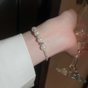 Close-up of multilayer pearl bracelet with diamond accents worn while holding a wine glass