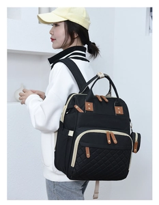 Side view of a stylish black quilted diaper backpack worn by a model in a white jacket