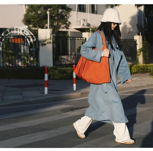 Street style view of a large orange nylon tote bag paired with a blue casual coat