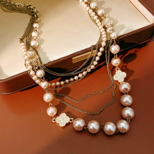 Detail of multi-layer pearl necklace featuring zircon-encrusted clover charms in gold