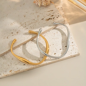 Irregular C-shaped stainless steel cuffs in gold and silver on a travertine stone