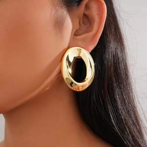 Close-up of a large polished gold oval hoop earring worn by a model for a modern look