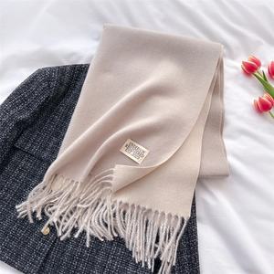 Flat lay of beige cashmere blend scarf with tassels on a grey tweed coat and tulips