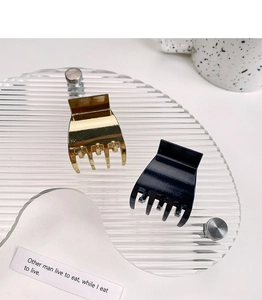 Close-up of small square hollow metal hair claws in gold and black on a textured tray