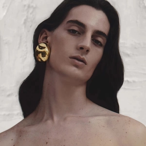 Detailed view of large gold oval stud earrings with textured hammer finish on female model