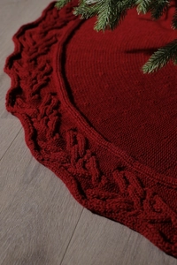 Close-up of dark red knitted Christmas tree skirt featuring a textured cable knit pattern